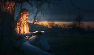 Man reads book at night sitting under tree